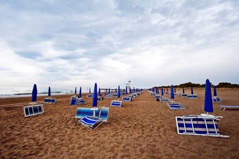 Folded deck chairs and parasols on a beach by the sea with rain clouds