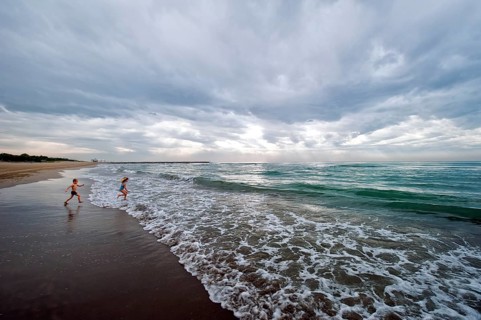 Two children running into the ocean with clouds providing a threatening mood