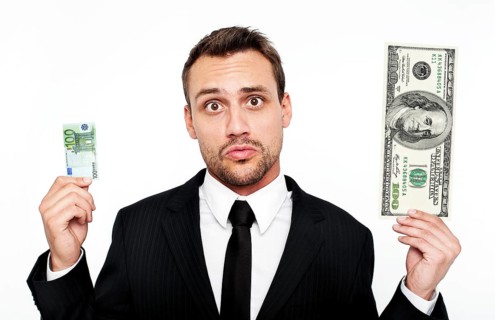 Frustrated young man wearing a suit holding a small 100 euro banknote and a large 100 dollar bill