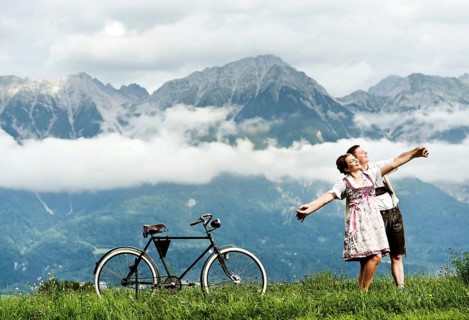 Man and a woman wearing traditional costume with an old bicycle within a natural landscape
