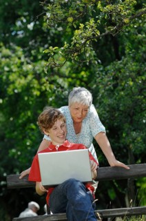 Grandson and grandmother looking together at a laptop computer on a park bench