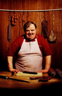 Fat butcher smiling with his hands propped on a bench in a butcher's store with a wooden ambience