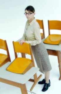 Strict female teacher standing at old school desks with orange chairs