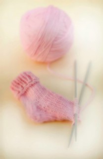 Semi-finished knitted pink baby sock with a ball of wool and knitting needles