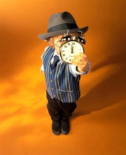 Boy wearing business clothes holding an alarm clock showing eleven fifty-five