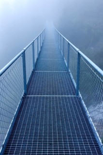 Steel bridge in the fog crossing over an Alpine stream