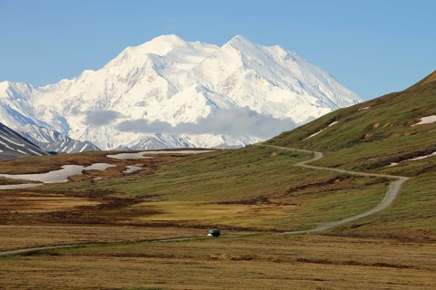 A shuttle bus from the Denali National Park and Preserve crossing the tundra with views of Mt McKinley at back