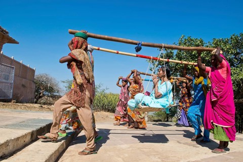 Young Indian women wearing traditional saris carrying long bamboo poles on their heads with a seat for pilgrims climbing the steps to the temple complex