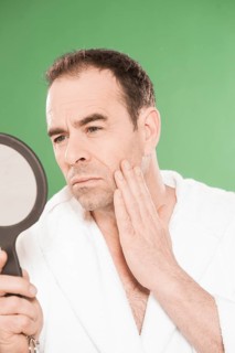 Man wearing a bathrobe observing himself critically in a hand mirror