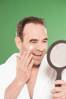Man wearing a bathrobe looking at himself in a hand mirror