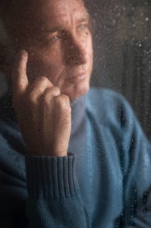 Lonely man sitting behind a window covered in rain drops