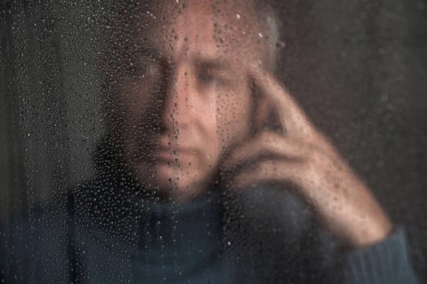 Lonely man sitting behind a window covered in rain drops