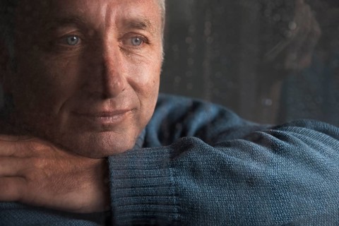 Lonely man sitting behind a window covered in rain drops