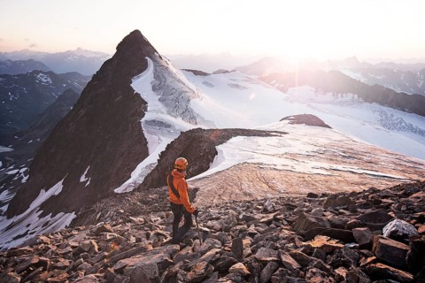 Mountain climber standing at the summit of Wilder Pfaff Mountain and looking towards the sunset