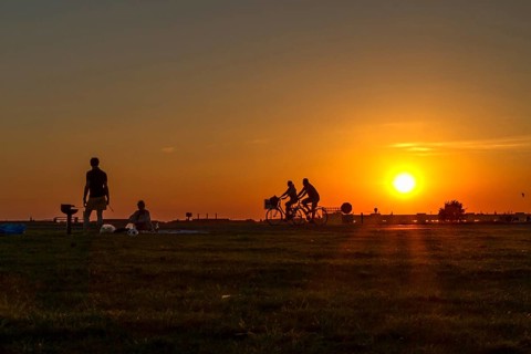 Couple having a barbecue on Tempelhof Airfield in the evening sun in front of two passing cyclists