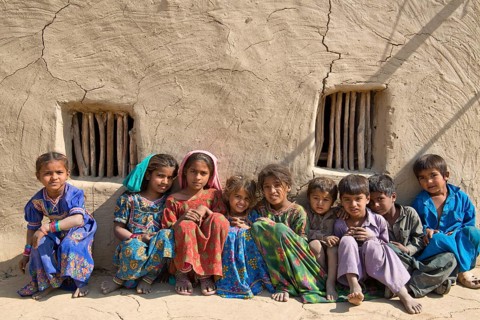 Children sitting in front of a mudbrick house