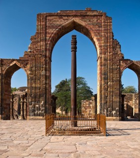 Entrance portal of the Quwwat-ul-Islam Masjid Mosque with relief decorations and an iron pillar in the courtyard