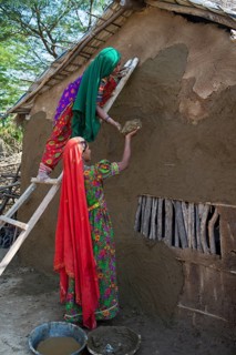 Two women wearing traditional saris rendering a house wall with a mixture of clay