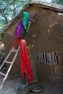 Two women wearing traditional saris rendering a house wall with a mixture of clay