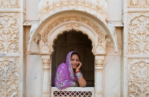 Young friendly Indian woman wearing a headscarf looking out of a window opening of an ornate marble facade