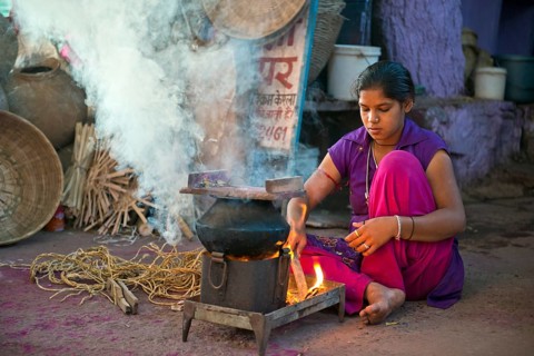 Young Indian woman squating on the ground and preparing a meal on a hotplate