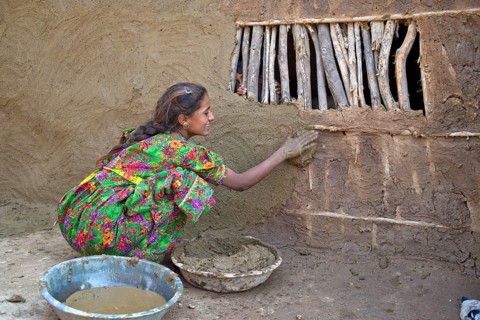 Girl in traditional dress plastering the wall of a house with a mixture of water