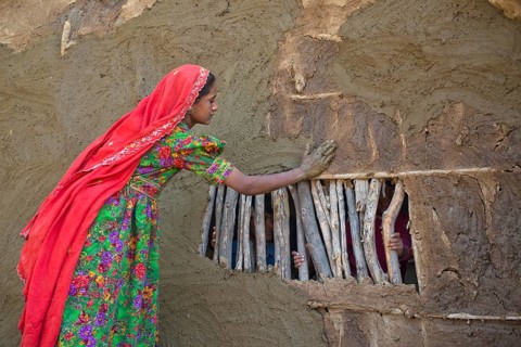 Girl in traditional dress plastering the wall of a house with a mixture of water