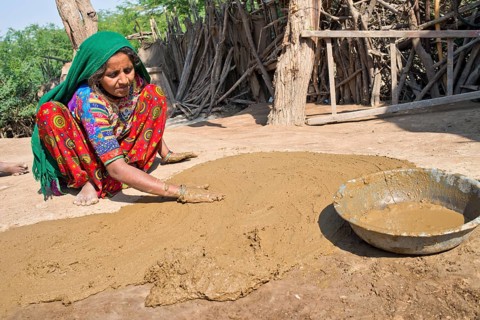 Woman in traditional dress plastering the floor of a courtyard with a mixture of water