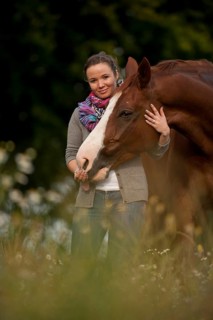 Woman standing next to a Hanoverian horse in a meadow