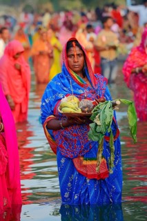 Woman wearing a blue sari with offerings standing in water during the Hindu Chhath Festival