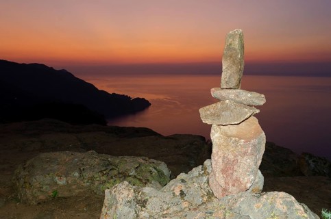 A typical cairn in the Calanche of Piana in front of a colorful sunset sky illuminated by a flash unit. The Calanche of Piana is in the western part of the island Corsica