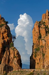 The typical bizarre red rocks of the Calanche of Piana below a blue sky and some clouds. The Calanche of Piana is in the western part of the island Corsica