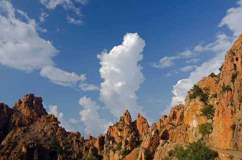 The typical bizarre red rocks of the Calanche of Piana below a blue sky and some clouds. The Calanche of Piana is in the western part of the island Corsica