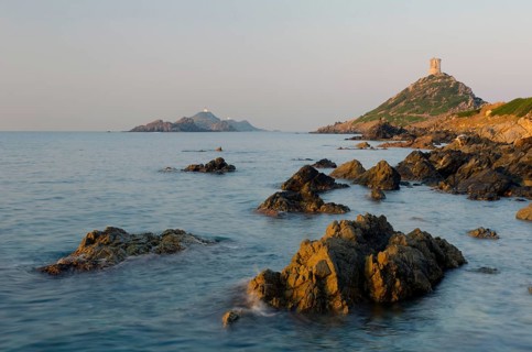 The genoese tower Tour de la Parata at the right and the islands Les Iles Sanguinaires behind the rocky mediterranean coast illuminated by warm morning light. Les Iles Sanguinaires are in the departme...