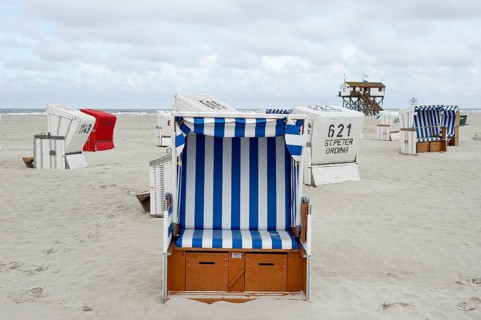 Roofed wicker beach chairs on the beach in front of a house on stilts