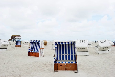 Roofed wicker beach chairs on the beach in front of a house on stilts