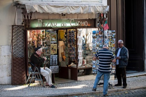 Souvenir vendor outside his shop with customers on the Largo do Carmo square