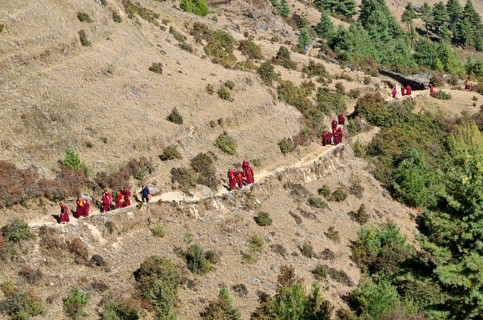 Monks and nuns wearing red cloths walking on a small path along a mountain slope