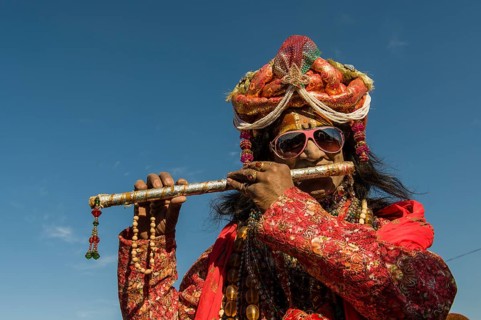 Colourfully costumed devotee playing flute during Kumbh Mela