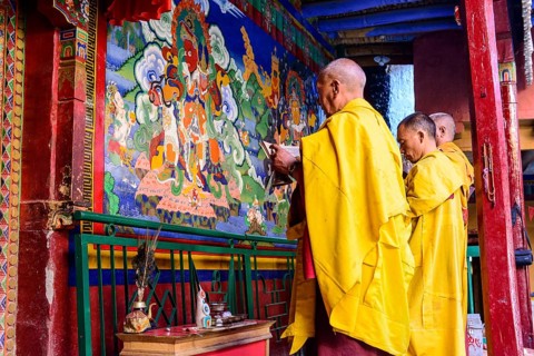 Three monks of Lamayuru Gompa are praying in front of a colorful religious wall painting