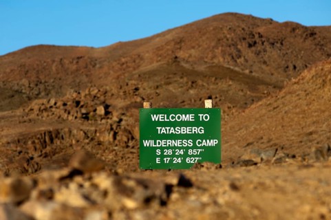 Welcome sign visible between rocks with GPS location information at the entrance of the Tatasberg Wilderness Camp