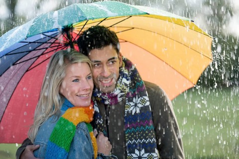 Smiling couple with a colourful rainbow umbrella is enjoying the rain