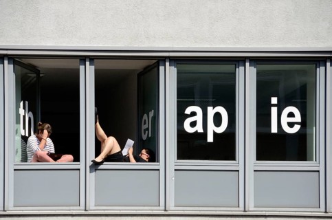 Students of a school for physical therapy taking a break and reading at windows with the word "therapie"