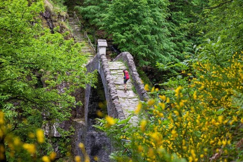 A woman hiking across the Ponte Romano bridge near Intragna