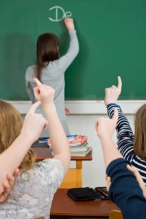 School children putting up their hands to answer in a classroom