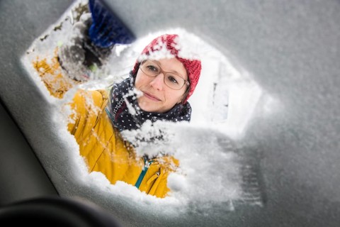 Young woman cleaning a car of ice and snow