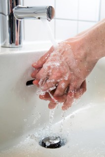 Person washing their hands under running water from a faucet