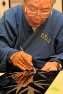Japanese artisan scraping the top lacquer coat away to carve out golden bamboo leaves