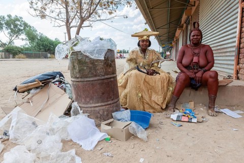Herero woman and Himba woman woman in traditional dress sitting next to rubbish
