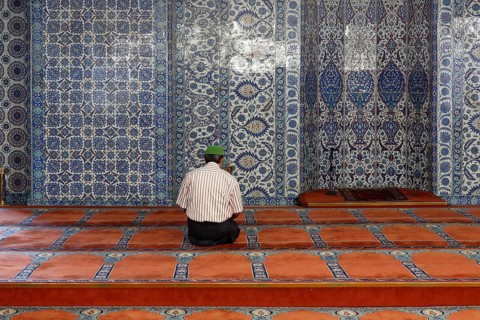 Man in prayer in front of a wall with Iznik faience tiles